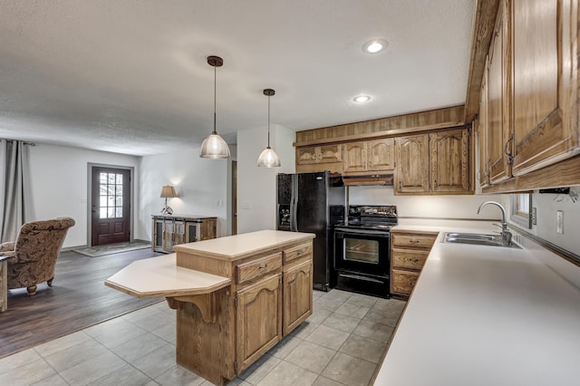 kitchen featuring a center island, light countertops, under cabinet range hood, a sink, and black appliances