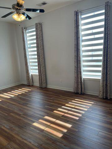 empty room featuring baseboards, ceiling fan, visible vents, and dark wood-type flooring