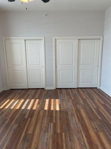 unfurnished bedroom featuring baseboards, dark wood-style flooring, a ceiling fan, and multiple closets