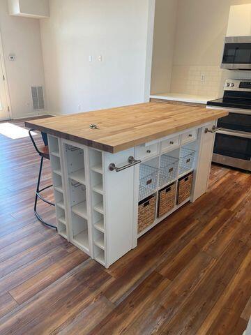 kitchen featuring open shelves, appliances with stainless steel finishes, dark wood-style floors, and butcher block counters