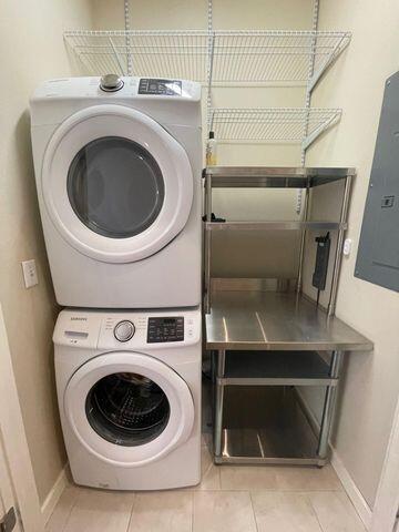 laundry area featuring laundry area, electric panel, tile patterned flooring, stacked washing maching and dryer, and baseboards