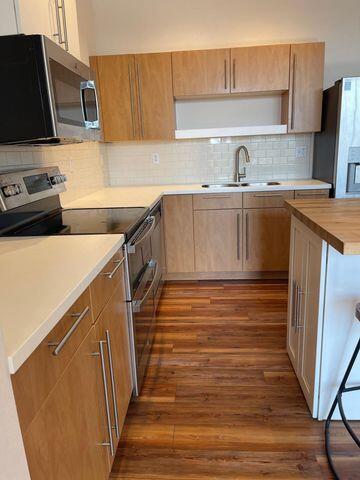 kitchen with appliances with stainless steel finishes, decorative backsplash, a sink, and dark wood-type flooring