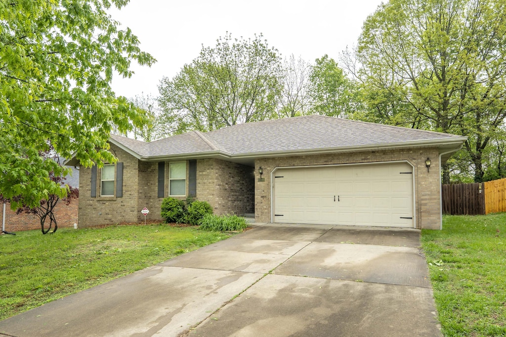 single story home featuring a garage, driveway, a front lawn, and brick siding