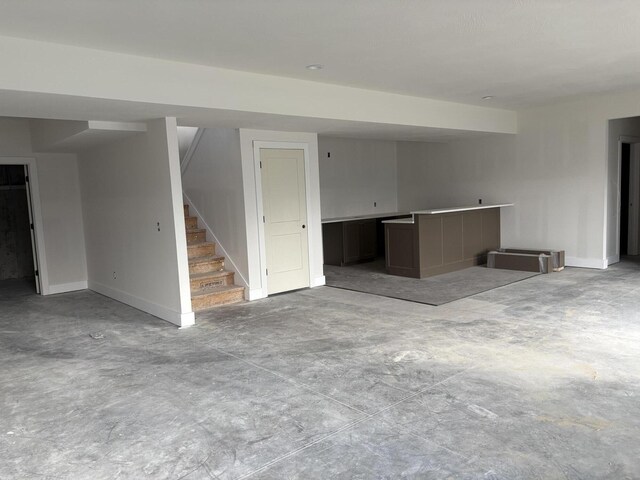 unfurnished living room featuring baseboards, stairs, and unfinished concrete flooring