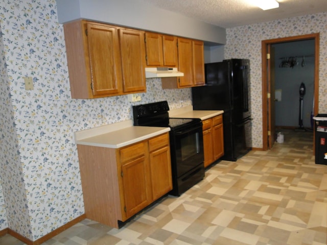 kitchen with light countertops, black appliances, wallpapered walls, and under cabinet range hood