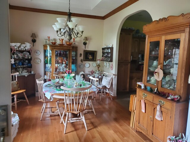 dining space with light wood-style floors, arched walkways, crown molding, and a chandelier