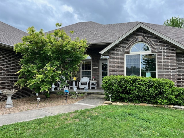 ranch-style home with brick siding, a shingled roof, a patio area, and a front yard