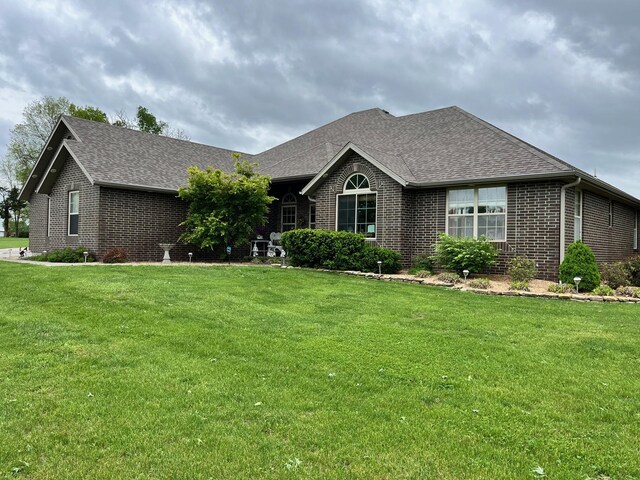 ranch-style home with a shingled roof, a front yard, and brick siding