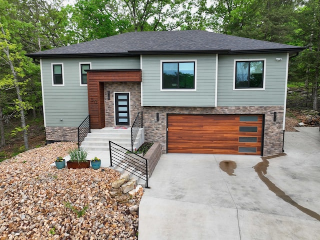 split foyer home featuring roof with shingles, an attached garage, driveway, and stone siding