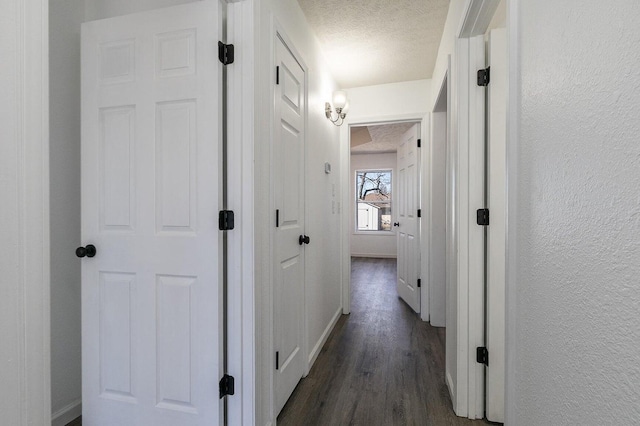 corridor featuring a textured wall, dark wood-style flooring, and a textured ceiling