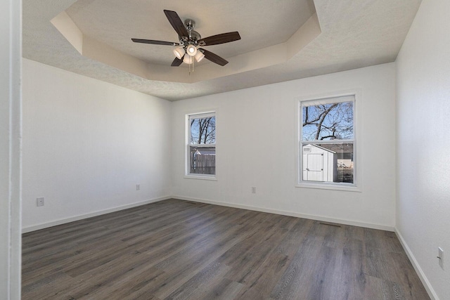 empty room featuring a healthy amount of sunlight, a raised ceiling, baseboards, and dark wood finished floors