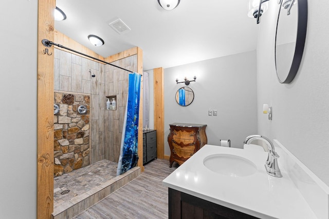 full bathroom featuring visible vents, vanity, wood finished floors, and tiled shower