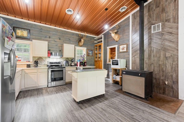 kitchen featuring visible vents, appliances with stainless steel finishes, wood walls, light countertops, and white cabinetry