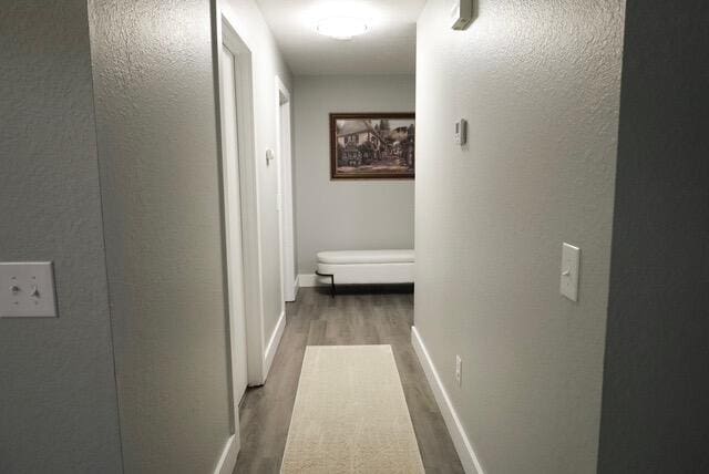 hall with baseboards, a textured wall, and wood finished floors