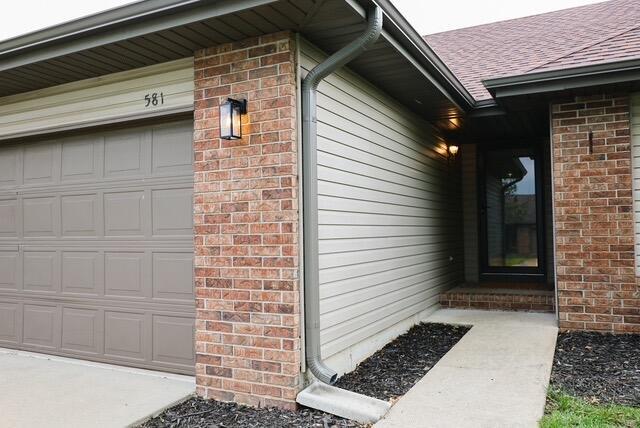 doorway to property with roof with shingles and brick siding