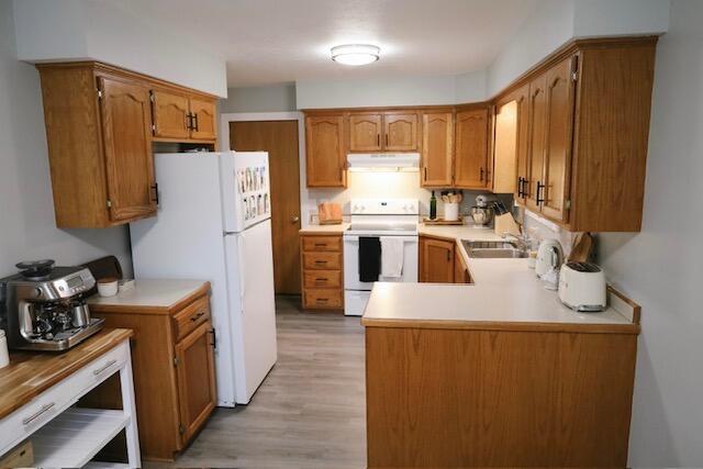 kitchen with brown cabinets, a sink, white appliances, light countertops, and under cabinet range hood
