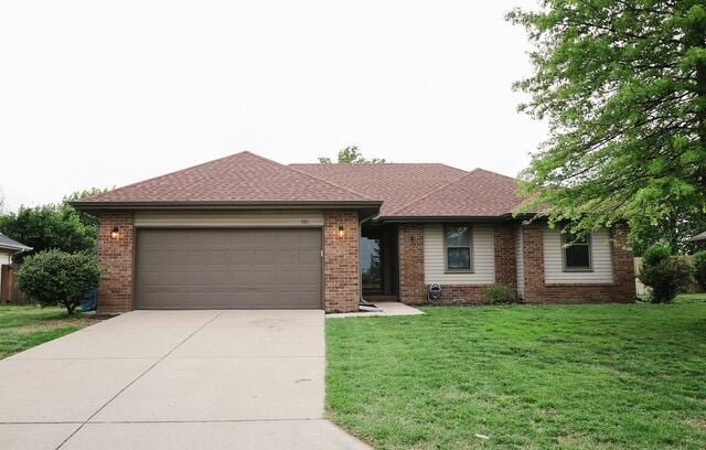 single story home featuring brick siding, a front lawn, an attached garage, and driveway