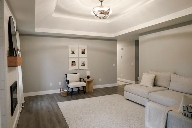 living room featuring baseboards, a glass covered fireplace, a raised ceiling, and dark wood-type flooring