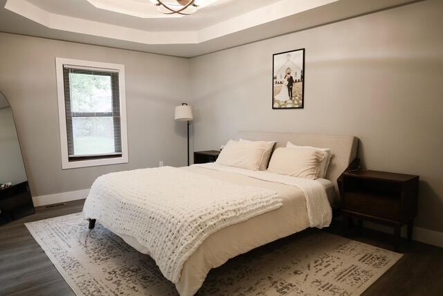 bedroom with baseboards, a raised ceiling, and dark wood-style flooring