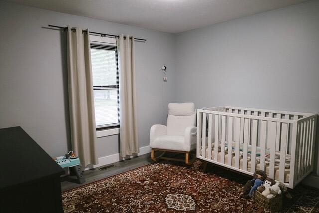 bedroom featuring a nursery area, baseboards, multiple windows, and wood finished floors