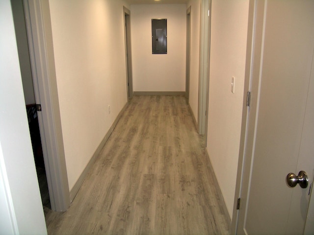 corridor featuring light wood-type flooring, baseboards, and electric panel