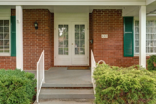 view of exterior entry with brick siding, covered porch, and french doors