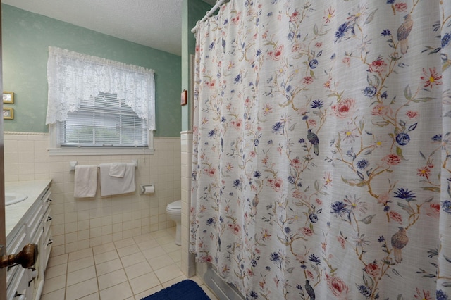 full bathroom featuring tile patterned flooring, tile walls, a wainscoted wall, toilet, and vanity