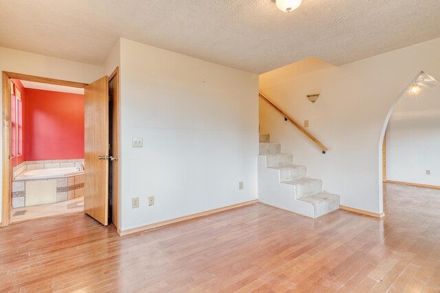unfurnished living room with stairway, baseboards, a textured ceiling, and wood finished floors