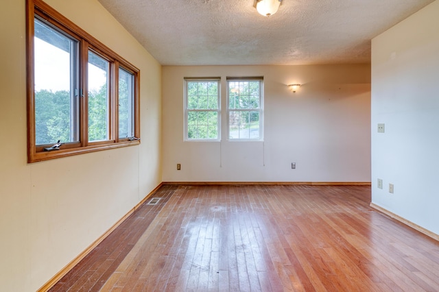 unfurnished room featuring baseboards, a textured ceiling, visible vents, and hardwood / wood-style flooring