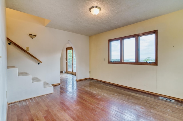empty room featuring stairway, arched walkways, wood-type flooring, and visible vents