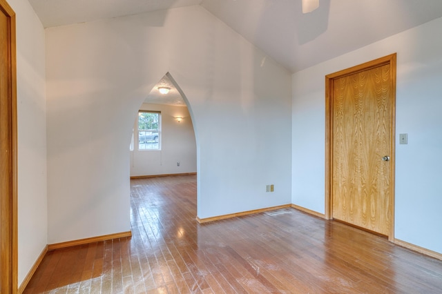 empty room featuring ceiling fan, arched walkways, baseboards, lofted ceiling, and hardwood / wood-style floors