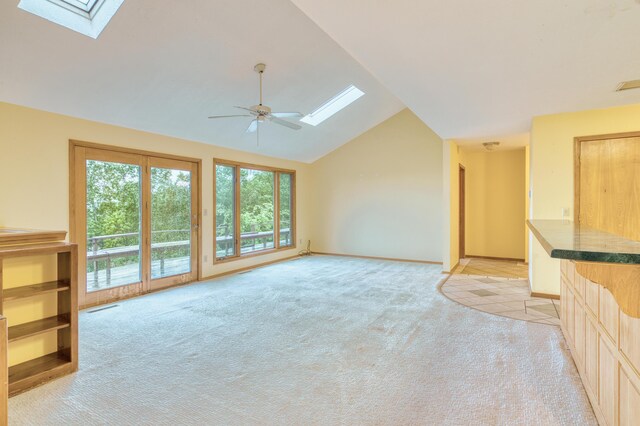 unfurnished living room featuring a ceiling fan, visible vents, light colored carpet, baseboards, and lofted ceiling with skylight