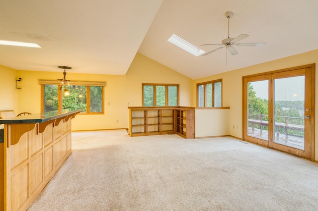 unfurnished living room featuring vaulted ceiling with skylight, baseboards, ceiling fan, and light colored carpet