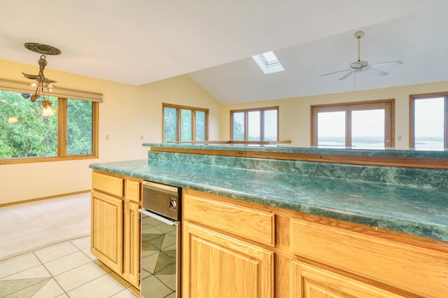 kitchen featuring light tile patterned flooring, dark countertops, light carpet, baseboards, and vaulted ceiling with skylight