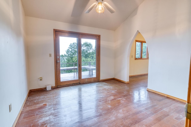 empty room featuring arched walkways, baseboards, a ceiling fan, and wood finished floors