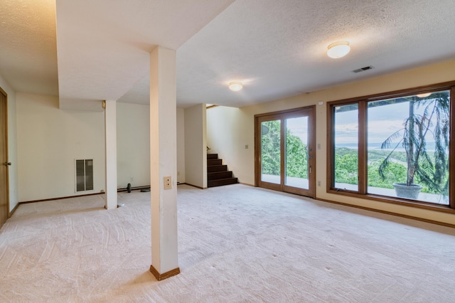 below grade area featuring light carpet, a textured ceiling, baseboards, visible vents, and stairway