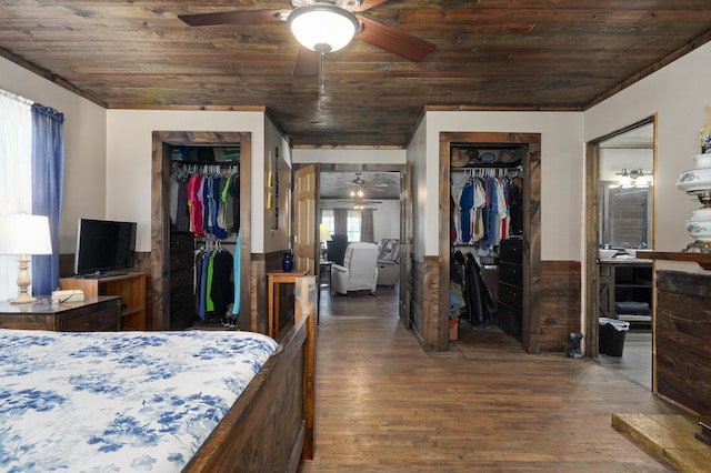 bedroom featuring ceiling fan, a walk in closet, a wainscoted wall, wooden ceiling, and wood finished floors