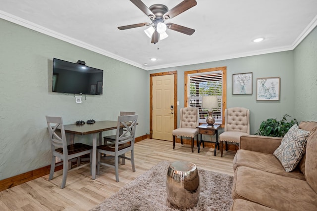 living area with a textured wall, light wood-style floors, a ceiling fan, baseboards, and ornamental molding