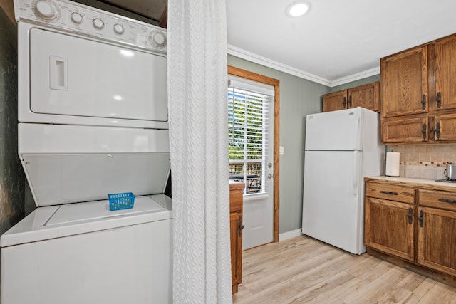 laundry room featuring crown molding, stacked washer / drying machine, laundry area, light wood finished floors, and baseboards