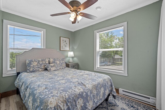 bedroom with a ceiling fan, crown molding, wood finished floors, baseboards, and a baseboard heating unit