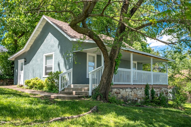 view of front of home featuring roof with shingles, covered porch, stucco siding, and a front lawn