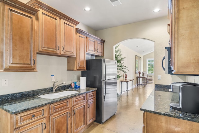 kitchen featuring freestanding refrigerator, arched walkways, brown cabinetry, and a sink