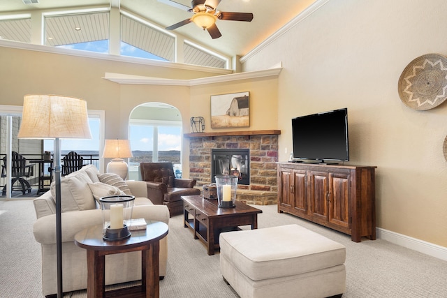 living area with a fireplace, high vaulted ceiling, light colored carpet, arched walkways, and a ceiling fan