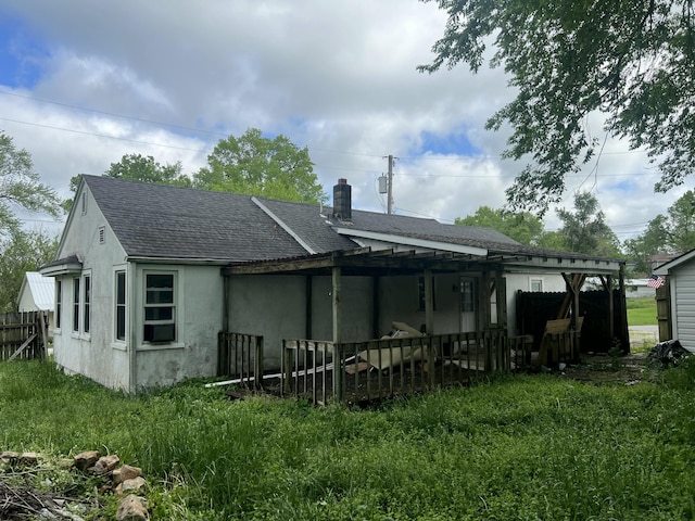 rear view of house with a chimney, a shingled roof, and stucco siding