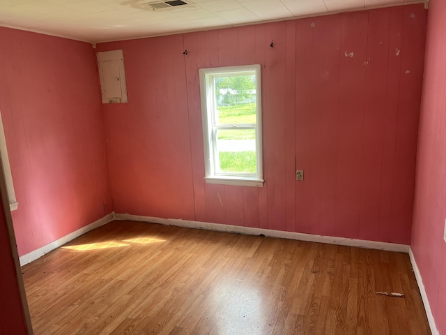 empty room featuring baseboards, electric panel, light wood finished floors, and visible vents