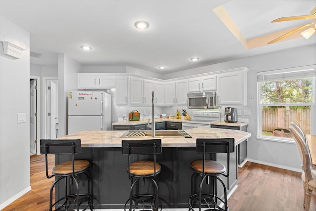 kitchen with a center island with sink, light wood-type flooring, baseboards, white appliances, and white cabinetry