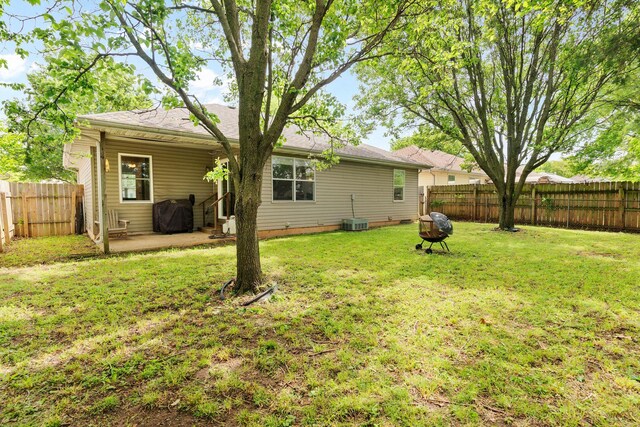 rear view of house with a fenced backyard, a patio, a lawn, and a fire pit