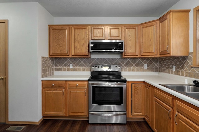 kitchen with light countertops, dark wood-style flooring, decorative backsplash, and stainless steel appliances