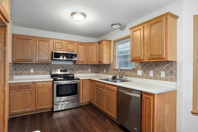 kitchen with light countertops, appliances with stainless steel finishes, a sink, and dark wood finished floors