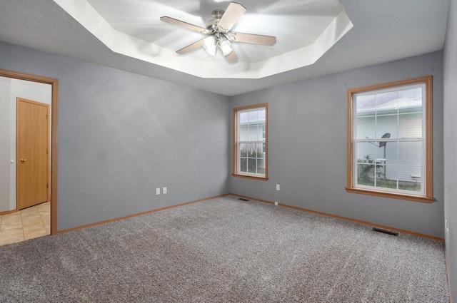 unfurnished room featuring light colored carpet, a raised ceiling, ceiling fan, and baseboards